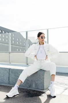 a woman sitting on top of a cement block wearing white pants and a blazer