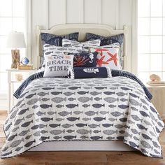 a bed covered in blue and white sheets with fish on the pillow cases, along with two lamps