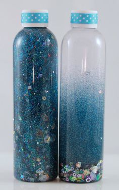 two bottles with blue glitter on them sitting next to each other