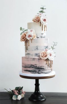 a three tiered cake with white and pink flowers on the top is sitting on a table