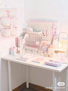 a white desk topped with lots of pink and white items next to a wall mounted light