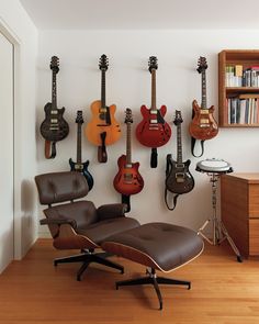 a room with guitars hanging on the wall and an eames chair in front of it