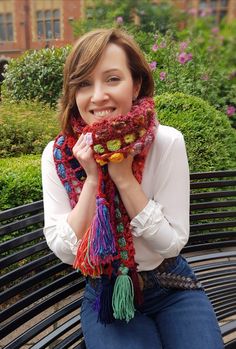 a woman is sitting on a park bench with her hands in her pockets and smiling