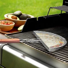 an outdoor grill with food cooking on it and bowls of vegetables in the back ground