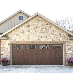 two brown garage doors in front of a brick house with three flower pots on the driveway