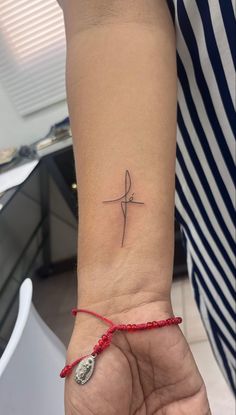 a woman's wrist with a small cross tattoo on her left hand and a red string around the wrist