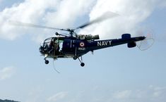 a navy helicopter flying through the air with its landing gear down