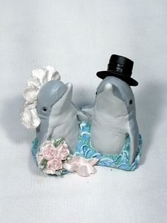 two dolphins with hats on their heads and one has a flower in its mouth while the other is wearing a top hat