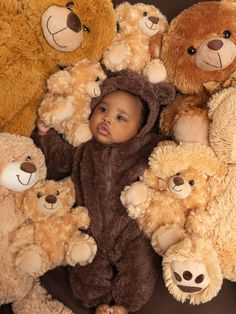 a baby in a bear suit surrounded by teddy bears on a brown background with the child's head between them