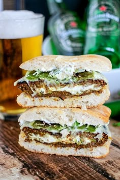 two sandwiches sitting on top of a wooden table next to a glass filled with beer