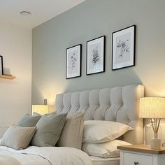 a white bed sitting next to two framed pictures on the side of a bedroom wall