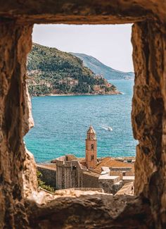 an old window with a view of the water and buildings in it, looking out to sea