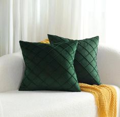 two green pillows sitting on top of a white couch next to a yellow throw blanket