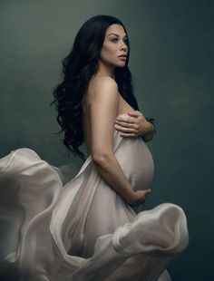 a pregnant woman in a flowing dress poses for the camera with her hands on her belly