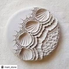 a white plate with shells on it sitting on top of a linen covered tablecloth