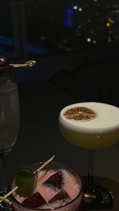 two cocktails are sitting next to each other on a table with the city lights in the background