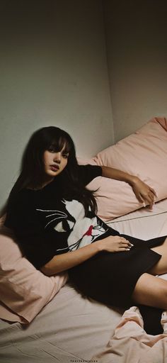 a woman sitting on top of a bed next to a pink comforter and pillows