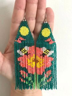 a pair of green and red beaded earrings with flowers on them, in the palm of someone's hand