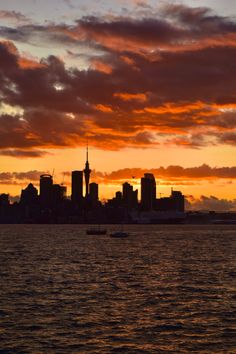 the sun is setting over a large city on the water with sailboats in the foreground