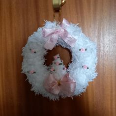 a white wreath with pink bows hanging on a door