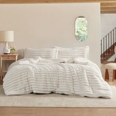 a bed with white comforter and pillows in a room next to a stair case