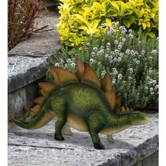 a toy dinosaur is walking on some steps in front of flowers and bushes with yellow flowers behind it