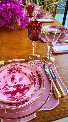 the table is set with pink and gold plates, silverware, and purple flowers