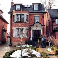 a red brick house with snow on the ground and trees in front of it,