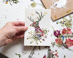 a person holding up a piece of paper with flowers on it and a deer's head