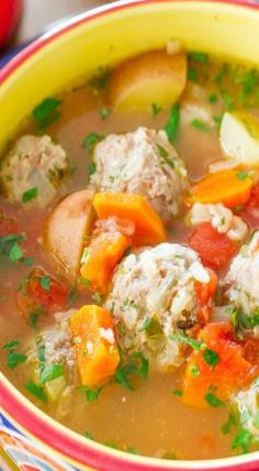 a yellow bowl filled with meatball soup on top of a wooden table next to an apple