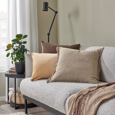 a couch with several pillows on it next to a lamp and a plant in a vase