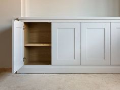 an empty room with white cupboards and beige carpeted flooring on the ground