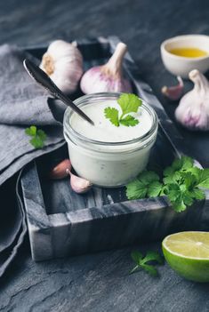 a small jar filled with white sauce next to garlic, lime and cilantro