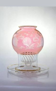 a pink glass vase sitting on top of a saucer next to a white wall