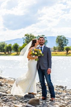 a bride and groom standing on rocks by the water