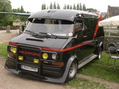 a small black truck parked on top of a grass covered field next to a building