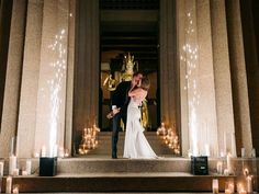 a bride and groom kissing on the steps of a building with candles in front of them