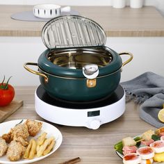 a big green pot is sitting next to some food on a table with other plates and utensils