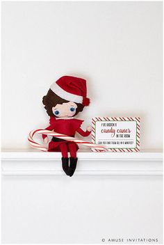 a red and white elf doll on top of a shelf next to a candy cane