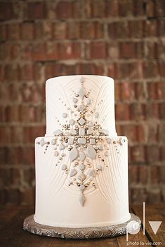 a white wedding cake sitting on top of a wooden table next to a brick wall