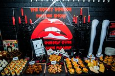 a table topped with lots of food next to a black wall covered in posters and candles