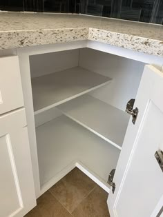 an open cabinet in a kitchen with marble counter tops