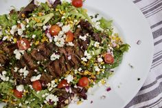 a white plate topped with meat and salad on top of a striped table cloth next to a fork