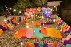 an outdoor wedding setup with bright colored linens and decorations on the ground, surrounded by lights