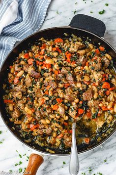 a skillet filled with beans, sausage and spinach on top of a marble counter