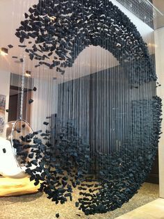 a sculpture made out of black beads hanging from the side of a glass wall in front of a window