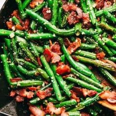 asparagus and bacon cooking in a skillet on a white table with silverware