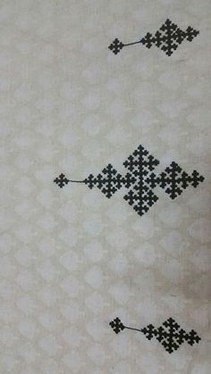 two black and white cross stitchs are on the table cloth, one has an arrow in it