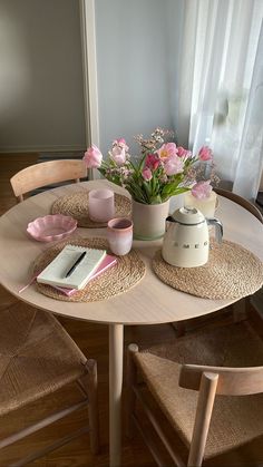 a wooden table topped with pink flowers next to a potted plant and a notebook