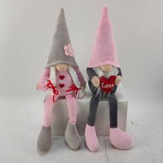 two small stuffed gnomes sitting next to each other on a white surface with one holding a heart